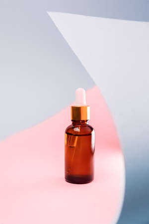 Close up of brown glass cosmetic bottle with dropper on a pink and gray background with abstract decor. The concept of an advertising template for beauty products.の写真素材