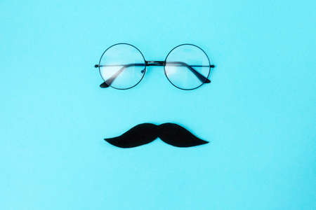 A felt mustache and eyeglasses on blue background with glasses. top view. Concept of Father's day...