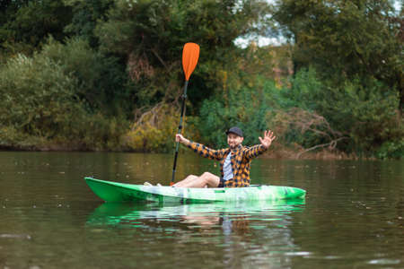 Kayaking on the river. Adult bearded caucasian man is sitting in a kayak and greetings. The concept of the water activities.の写真素材