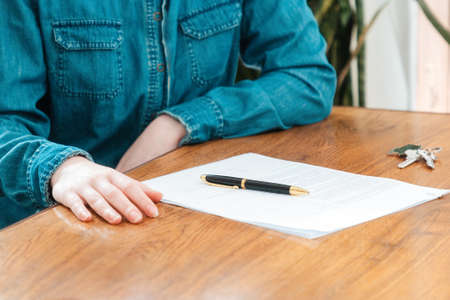 A client in a denim shirt is sitting at a table with documents and keys. close-up. The concept of insurance, mortgage and rental of real estate.の写真素材