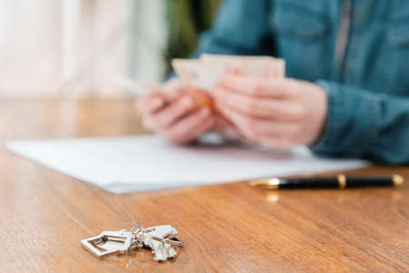 Close up of key with keychain lies on the table. Defocused person's hands counting money at the background. Concept of purchase of real estate and mortgage.の写真素材