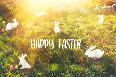 The concept of Easter holidays. Decorative handmade crafts in the form of white rabbits and colorful eggs. Grass in the background. Inscription Happy Easter. light.の写真素材