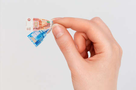 Woman's hand hold tiny banknotes of rubles. Isolated on a gray background. The concept of finance,...