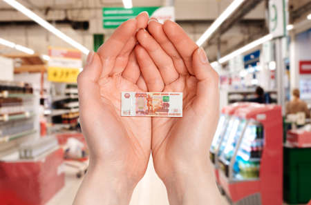 Close up of female palms holds a small five-thousand rubles banknote. Blurred store in the background. The concept of economic crisis and inflation.の写真素材