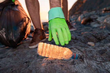Volunteer picks up a plastic bottle on the beach. close up of hand. low angle view. The concept of...