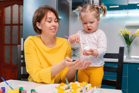 Easter celebration. Mother and her toddler daughter painting eggs. Little girl having fun with her mother.の写真素材