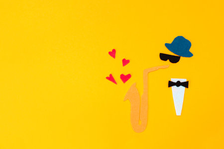 International Jazz Day. Silhouette of a musician with a saxophone, which hearts and flew out on a yellow background, cutted out of felt. copyspace. flat lay.の写真素材