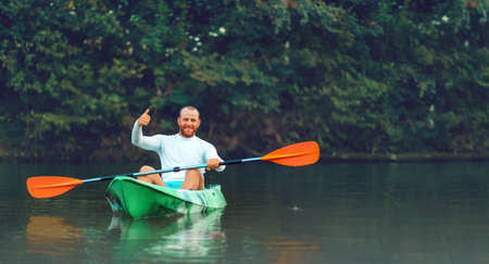 Kayaking on the river. Banner. An adult man is sitting in a kayak and gives a thumbs up. copyspace. The concept of the World Tourism Day.の写真素材