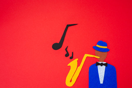 International Jazz Day. Silhouette of a musician with a saxophone from which melodies flew out, on a red background, cutted out of felt. flat lay. copyspace.の写真素材