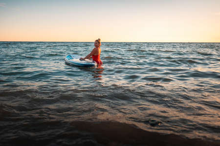 Pretty adult plump woman in a red swimsuit swimming in the sea with a sup board. copyspace. The...