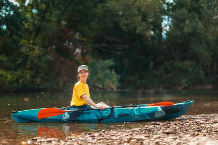 World Tourism Day. A young happy woman is sitting in a kayak on the river bank. copyspace. The concept of kayaking and outdoor activities.の写真素材