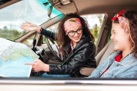 Automobile's trip. Smiling mother shows paper map to daughter sitting in a car. The concept of travel.の写真素材