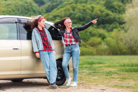 Automobile's trip. Happy caucasian woman and teen girl standing by a car. Park at the background. The concept of buying a new vehicle.の写真素材