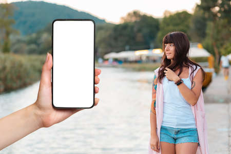 summer holiday. A females hand is holding a phone. Mock up. Beautiful woman with a tattoo on her...