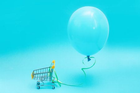 A blue balloon on a blue background with a small shopping cart. copyspace. The concept of holiday...