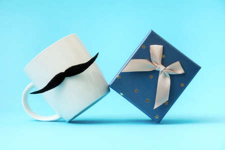 Close up of white mug with a felt mustache and present box on a blue background. Concept of Father's day.の写真素材