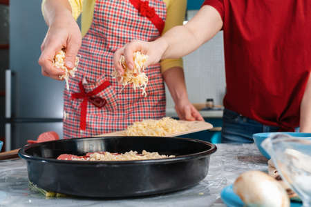Two women prepare pizza, sprinkling cheese on top of it. hands close up. The concept of homemade food.の写真素材