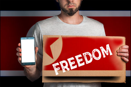 Concept of freedoms and human rights. A man with a cardboard and a phone in his hand. The Flag of North Korea. copy space and mock up.の写真素材