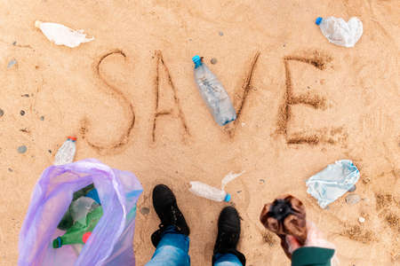 Volunteer stands on a sandy beach with trash bag. Text SAVE on coast. top view. The concept of environmental protection and pollution.の写真素材