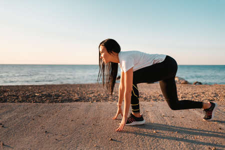 Sports and Jogging along the sea. A young brunette woman stands ready to run. In the background, the sea and the rocky shore. Horizontal. copyspace.の写真素材
