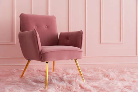 An elegant armchair upholstered in pink velvet, standing on a fluffy carpet. Modern luxury interior.の写真素材