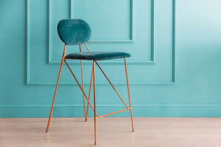 A stylish chair upholstered in turquoise velvet stands on the parquet floor.の写真素材