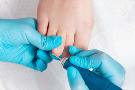 A pedicure master polishes the toe fingers with a mechanical device with a circle nozzle. close-up. top view. The concept of a professional nail care salon and chiropody.の写真素材