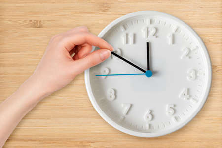 A woman's hand moves the hands of the clock, close-up. flat lay. wooden background. The concept of...