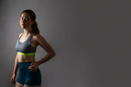 sport and health. A beautiful athletic young woman in gym clothes, hands on hips, looking tired. dark color. copyspace.の写真素材