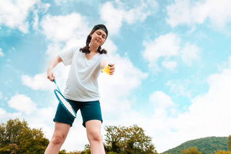 Pretty young woman holds a racket in her hand, preparing to hit a shuttlecock. bottom view. The sky is in the background. Badminton game and summer activity.の写真素材