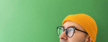 Close up face of young man with glasses and a hat looking at the left top side. Banner with copy space. The concept of choice, vision and searching.の写真素材