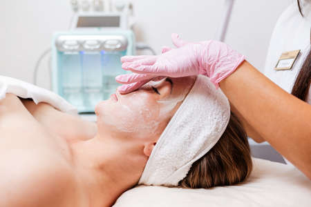 Cosmetologist's hands at protective gloves massages client's face with cosmetics mask. side view. Concept of professional cosmetology.の写真素材