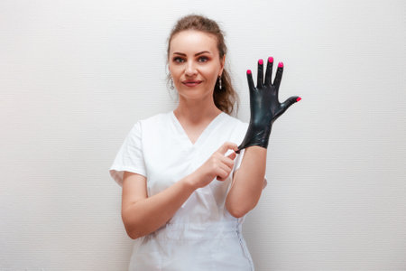 Portrait of a smiling manicurist woman wearing latex black glove with pink nailpolish. The concept of professional care of nails in beauty salon.の写真素材