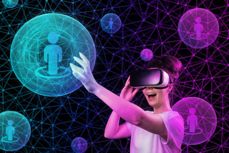Portrait of young happy woman in VR glasses touch a sphere with symbol of person. Dark background with abstract mesh and neon light balls. The concept of 3D simulation, and cyber space.の写真素材