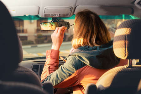 A woman is sitting in a car driving and doing makeup. rear view. The concept of emergencies and accidents on the road.の写真素材