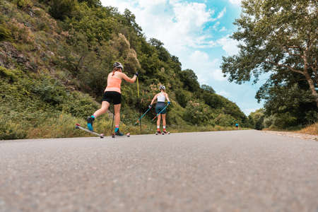 Two athletic women together training on the roller ski. Back low angle view. copyspace. Concept of competition, biathlon, and summer workoutの写真素材