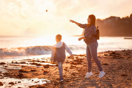 family time. A young mother and her son throw pebbles into the sea. In the background is the sea and sunset. The concept of a happy childhood and a single mom.の写真素材