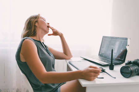 A young woman yawns in the workplace. Fatigue and overload in office work.