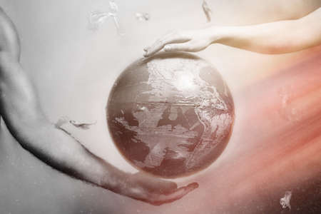 Women's and men's hands support the globe of planet Earth. Around the flying plastic debris. The concept of protecting the earth's environment.Red and white drammatic tint.の写真素材