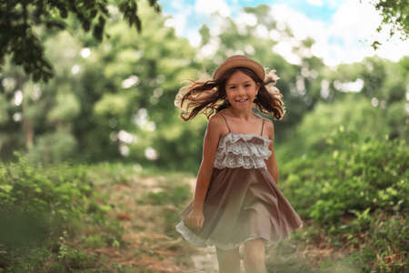 Portrait of smiing schoolgirl in a hat and dress runs in the park. Summer holidays. The concept of happy childhood and Children's Day.の写真素材