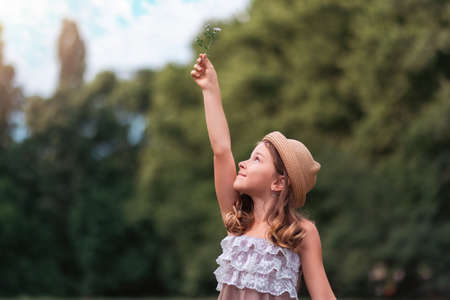 Portrait of a cute Caucasian small girl in a straw hat holding up a daisy flower. copyspace. The concept of peace, freedom, childhood, Earth Day and Summer.の写真素材