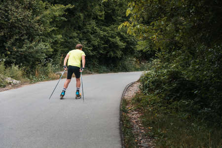 Hard training an athletic man on the roller ski, back view. Biathlon ride on the roller skis with...