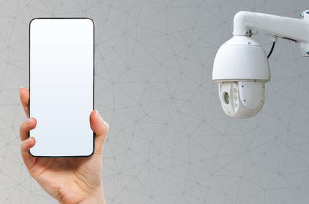 online supervision. Hand holding a smartphone with mock up and video surveillance camera. Gray...