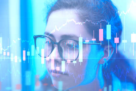 Investments and stock trading. Portrait of a young woman trader with glasses looking at index...
