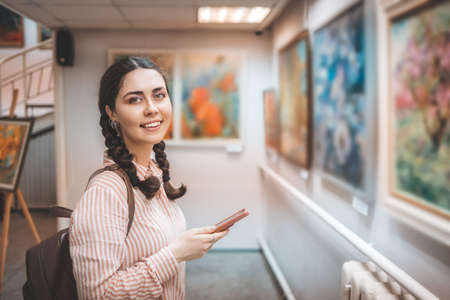 Portrait of smiling caucasian woman holding a smartphone. Excursion with audio guide in the art gallery. Exhibition and visit to the museum.の写真素材