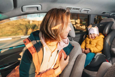 Smiling mother looking back to her cute happy little child is sitting at safe childrens backseat. The concept of safety during travel by car.の写真素材