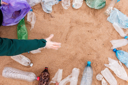 Volunteer picking up a garbage. Frame from plastic dirty bottles with copy space on a sandy beach. top view. The concept of environmental protection and ecology template.の写真素材