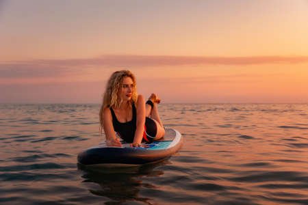Summertime and holidays. Sexy young woman posing lying at sup board in the ocean. copyspace. Sunset at the background. The concept of sea sport.の写真素材