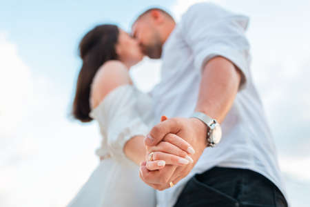 Valentine's day. Defocused kissing young couple of caucasians man and woman. hands close up. In the background blue cloudy sky. bottom view.の写真素材