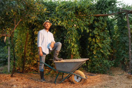 Handsome bearded gardener poses with his foot on a cart. Passion fruit plantations in the...
